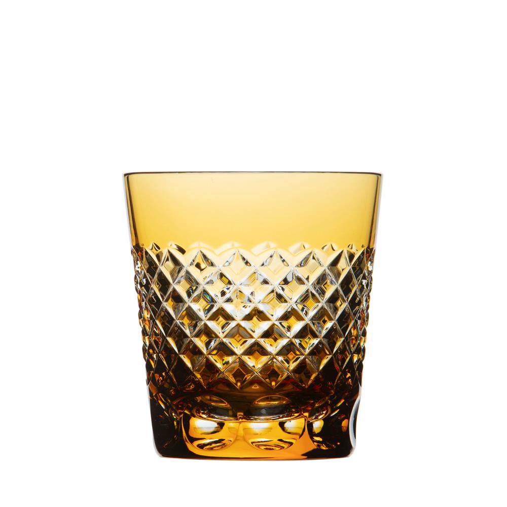 Amberfarbenes Trinkglas aus Kristallglas von ARNSTADT KRISTALL mit brillant handgeschliffenem Karomuster unten. Oberer Rand glatt, Glas durchscheinend. Facetten des mundgeblasenen Glases reflektieren elegant Licht auf Weiß.